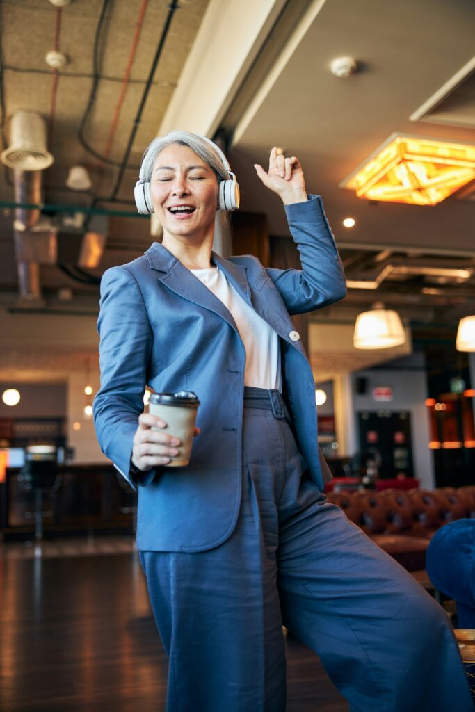 Joyful woman in blue suit dancing with coffee cup in a café, celebrating life