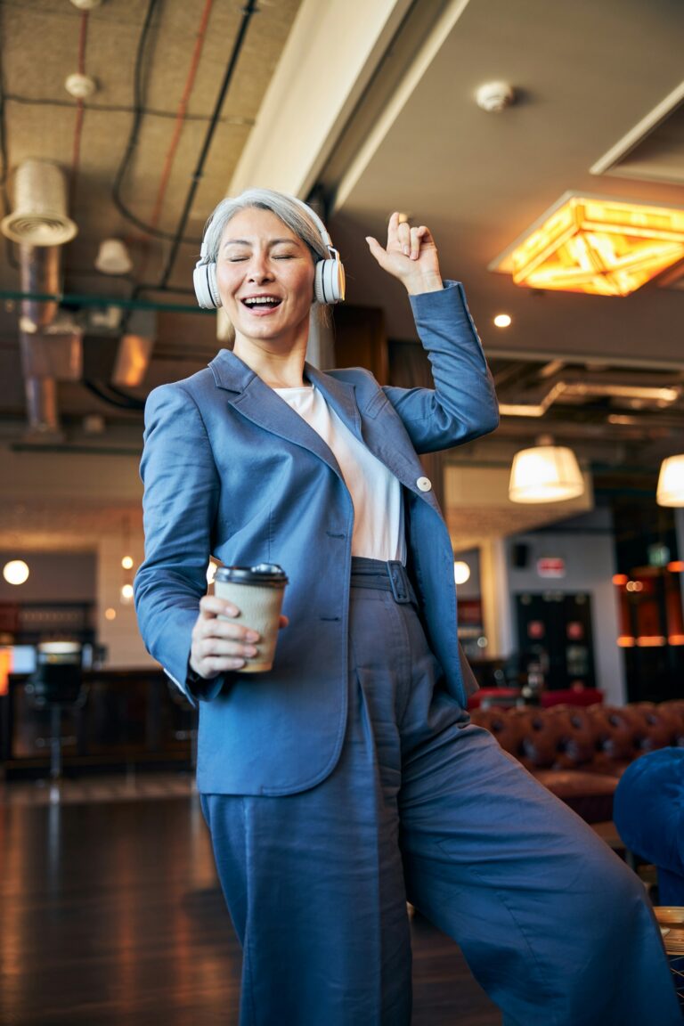 Joyful woman in blue suit dancing with coffee cup in a café, celebrating life